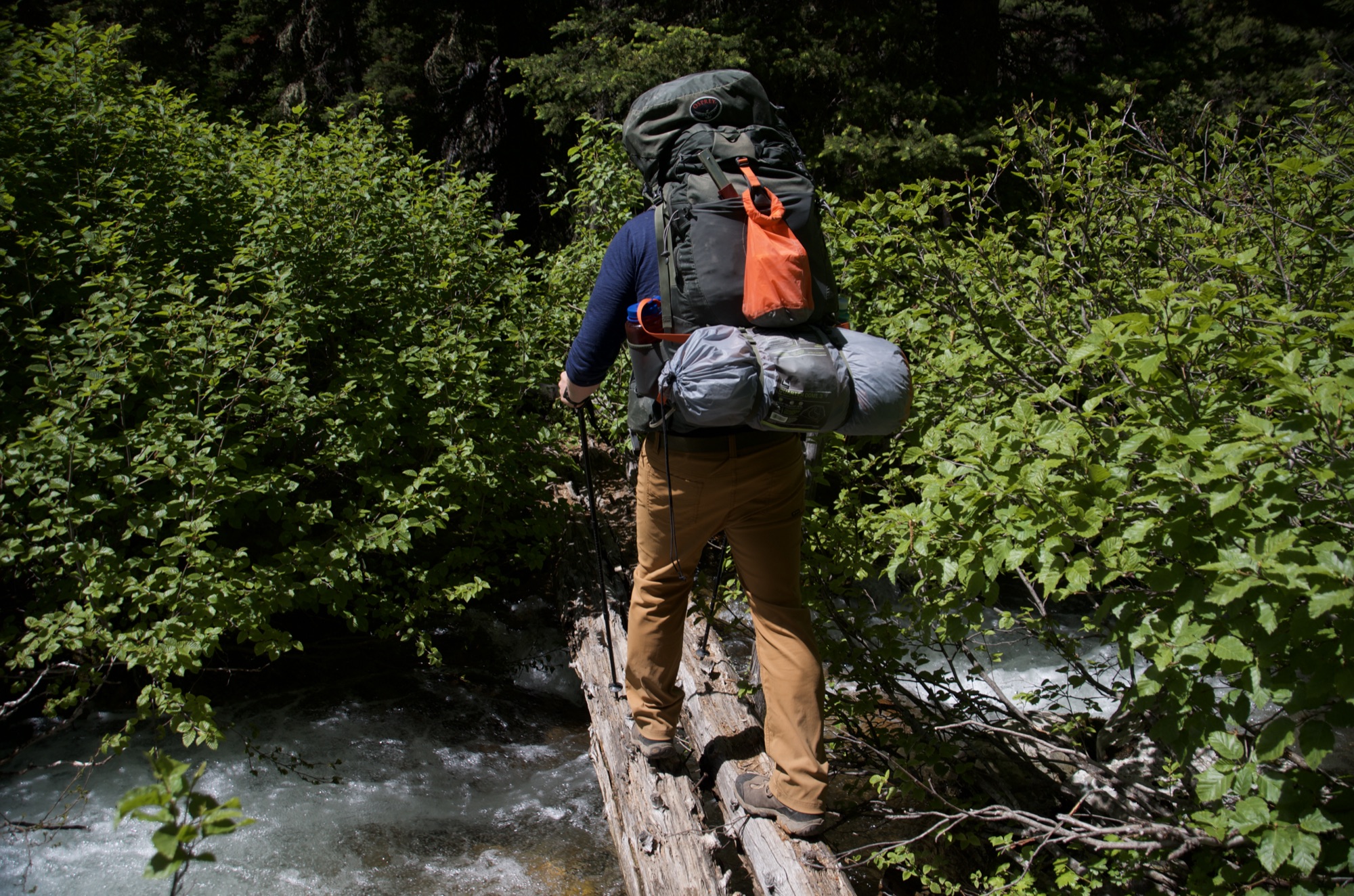 Backpacker balancing across log over rushing creek