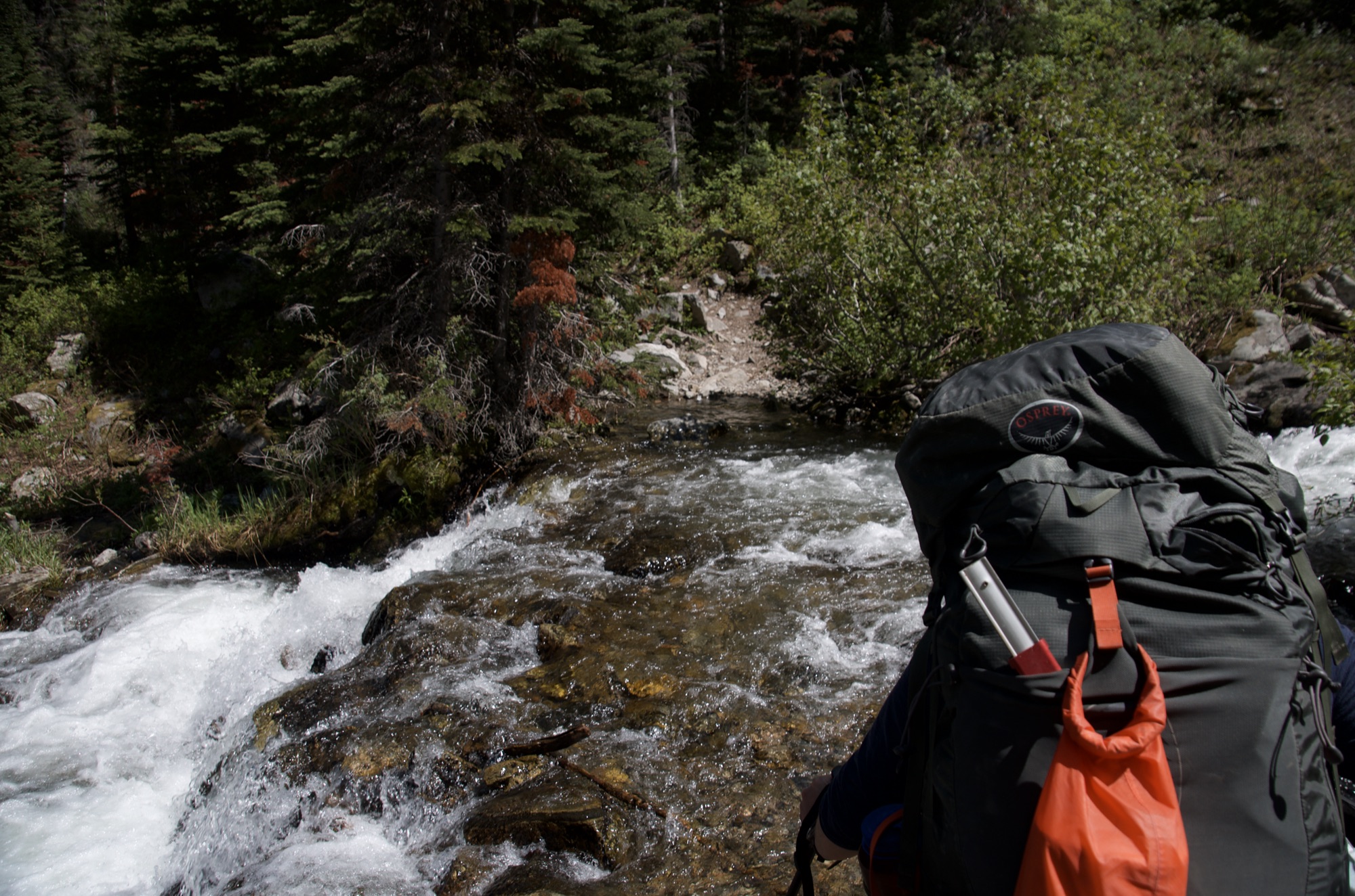Backpacker surveying rushing creek crossing with pack