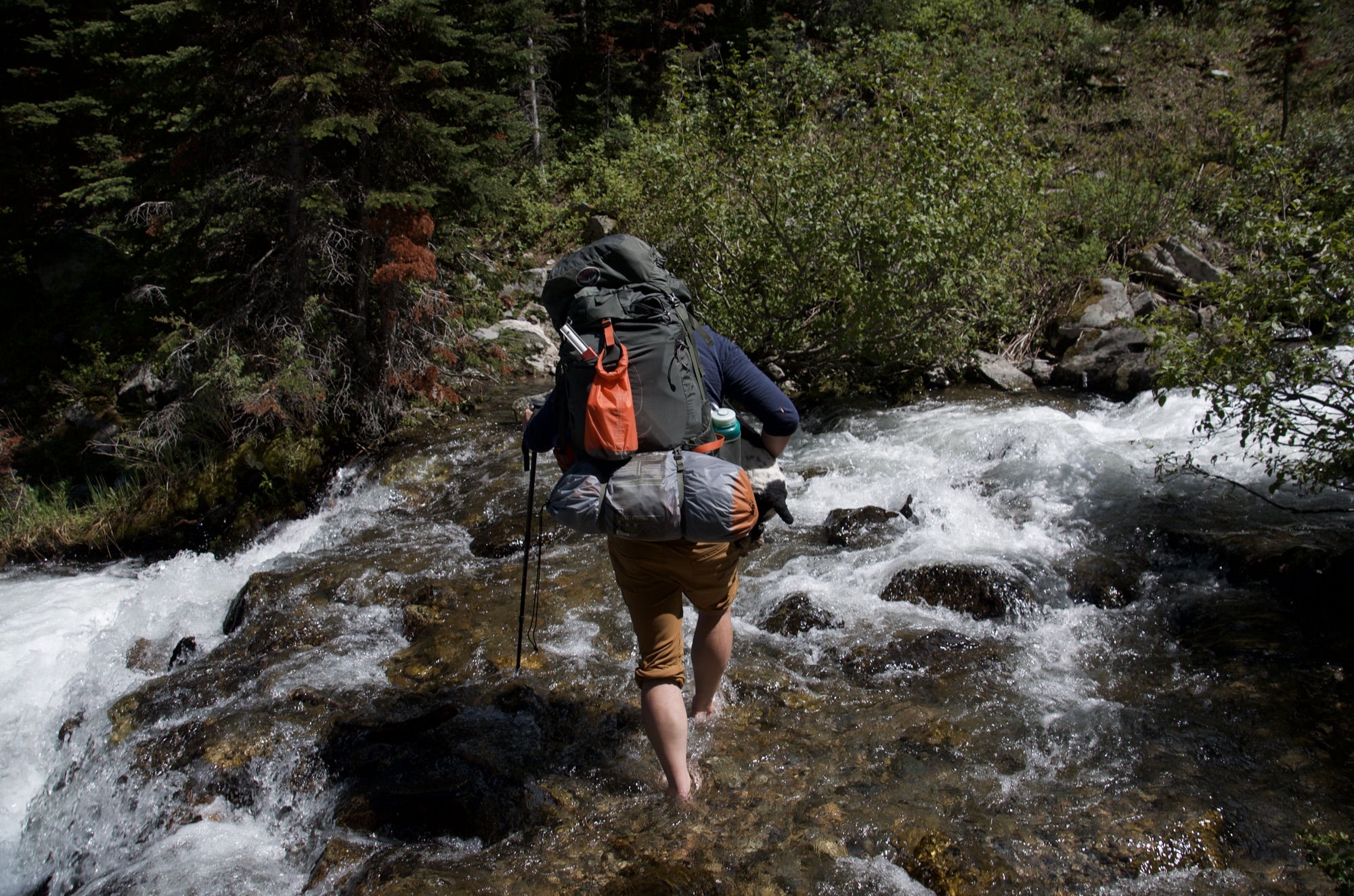 Backpacker crossing rushing creek barefoot with trekking pole