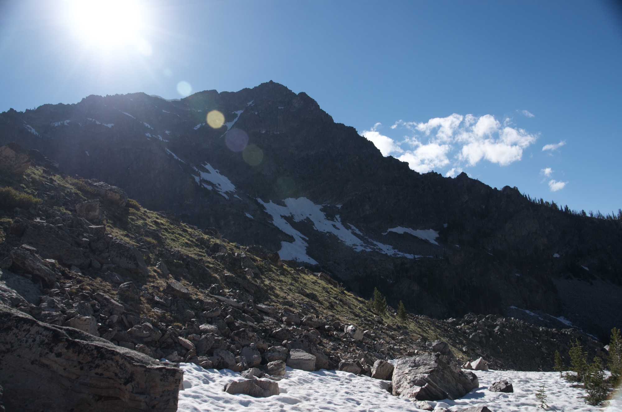 Rugged peak with snow patches and sun flare above rocky slope