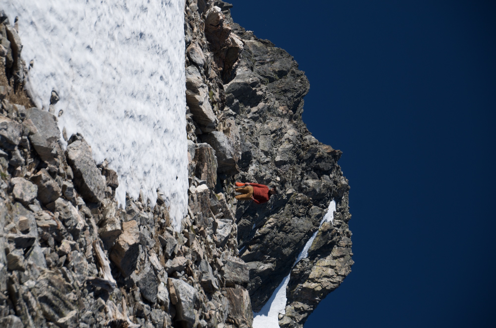 Hiker scrambling on rocky ridge above snowfield