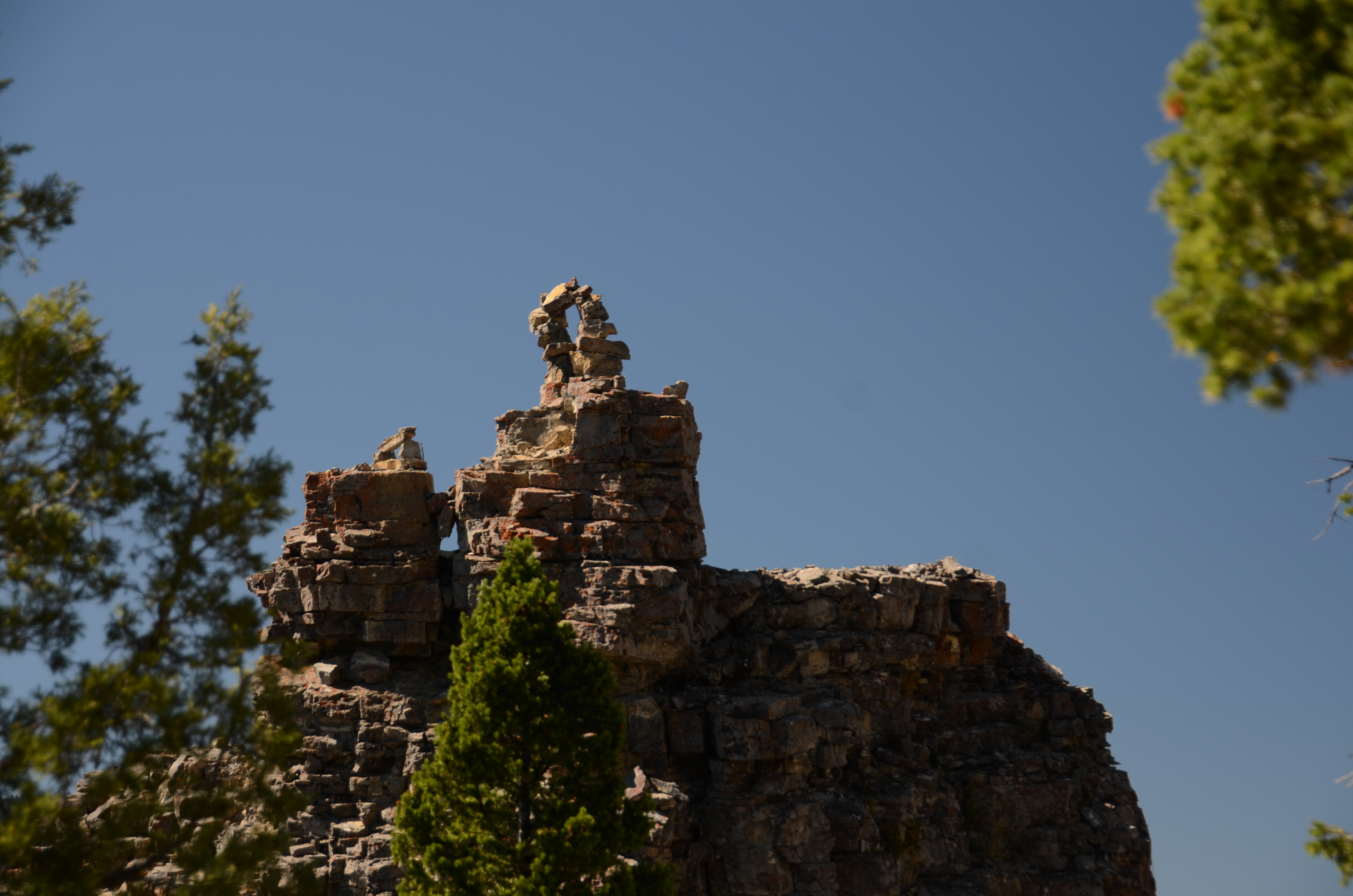 Storm Castle Peak limestone turret with natural arch on top framed by pine trees against a deep blue sky