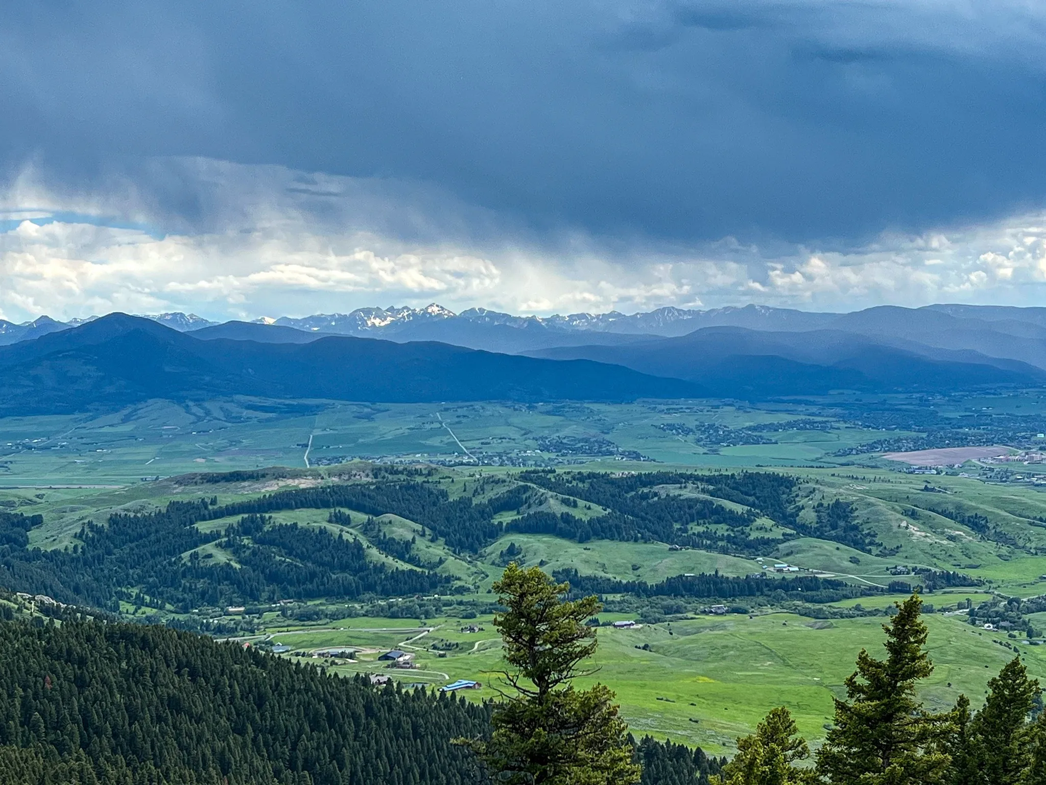 Wide Gallatin Valley view from Sypes Canyon with green foothills, distant mountains, and storm clouds