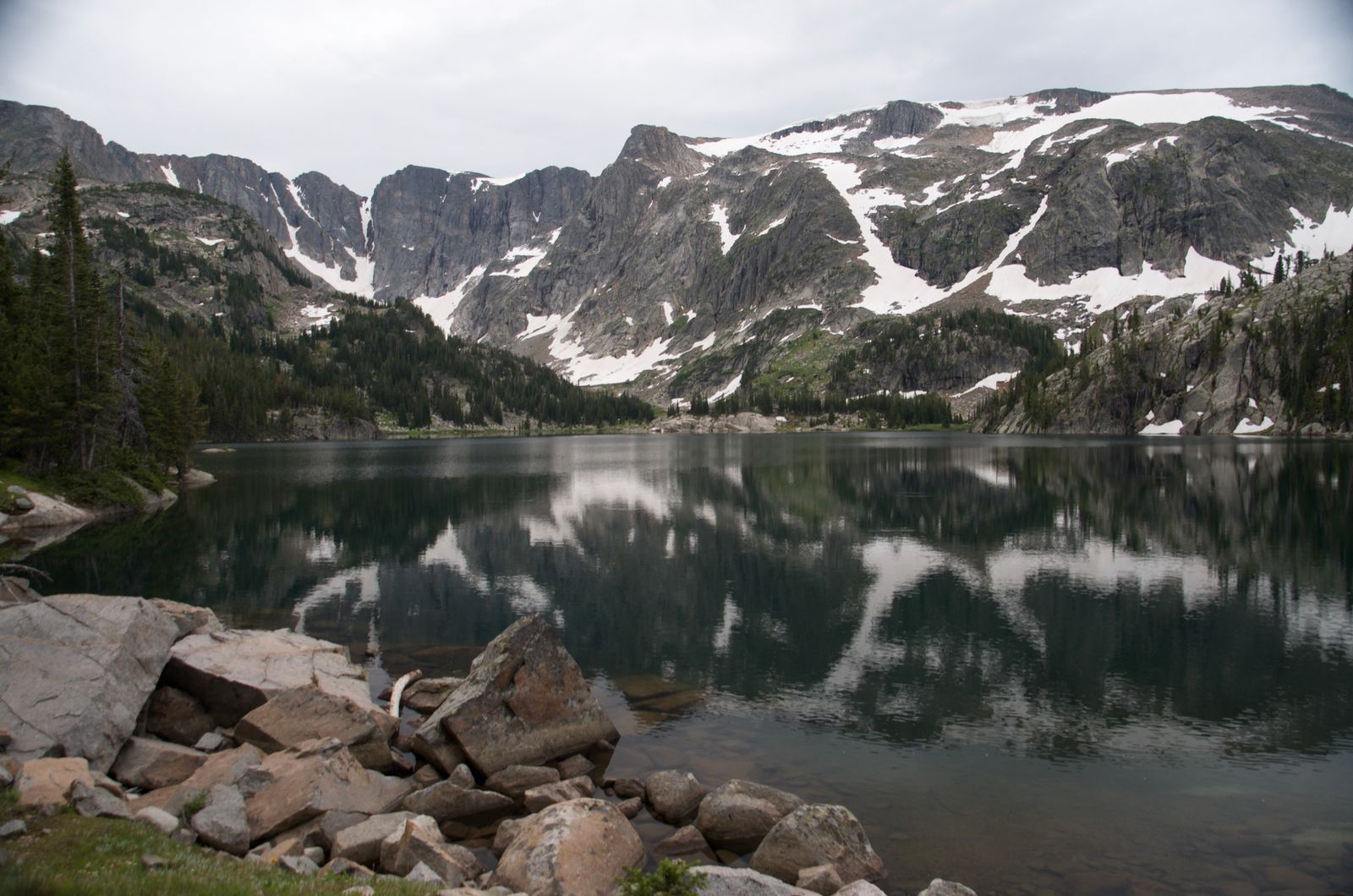 Alpine lake perfectly reflecting snow-patched Beartooth peaks on cloudy day