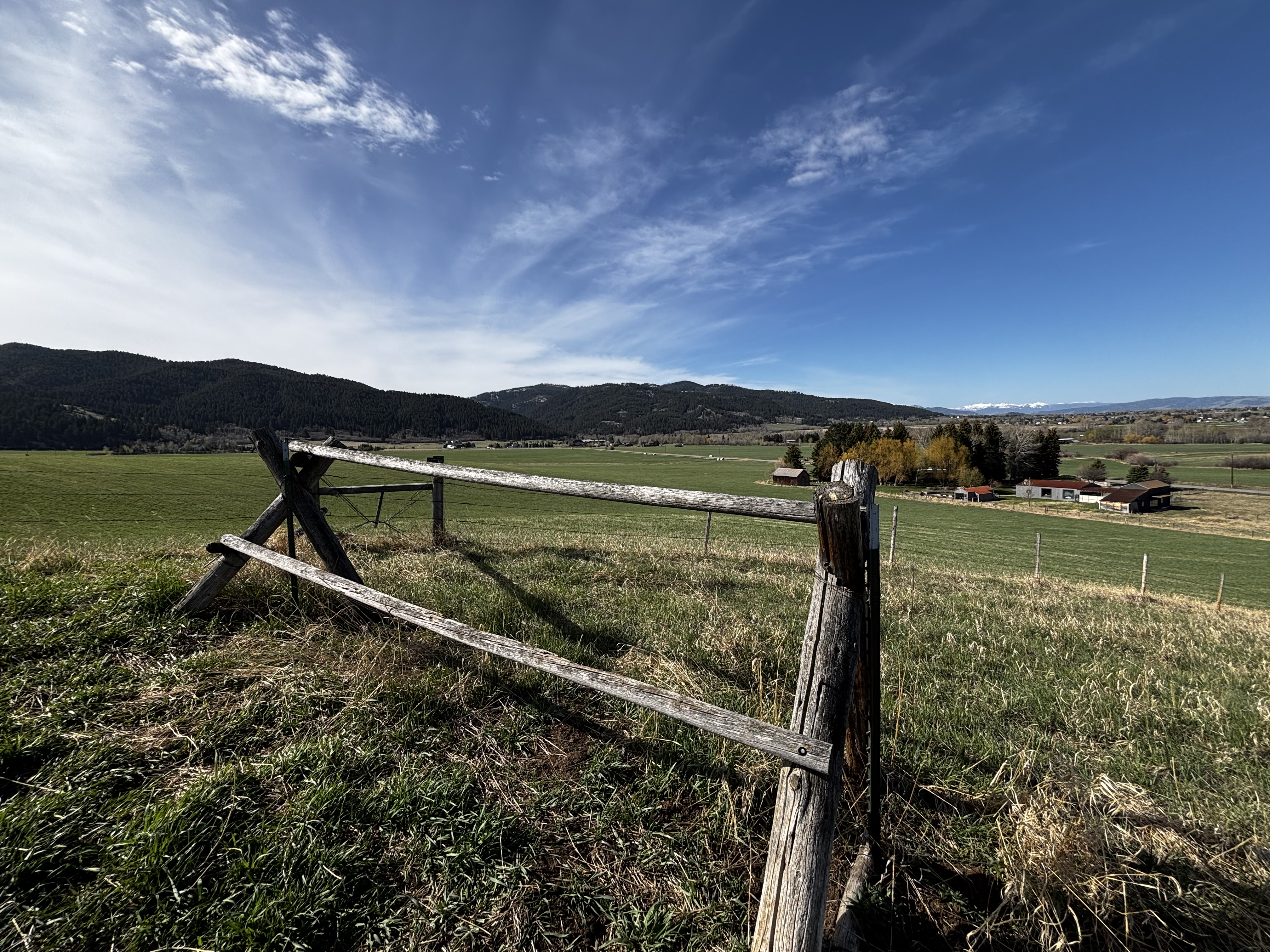 Weathered split-rail fence running across green rolling hills with forested mountains in the background