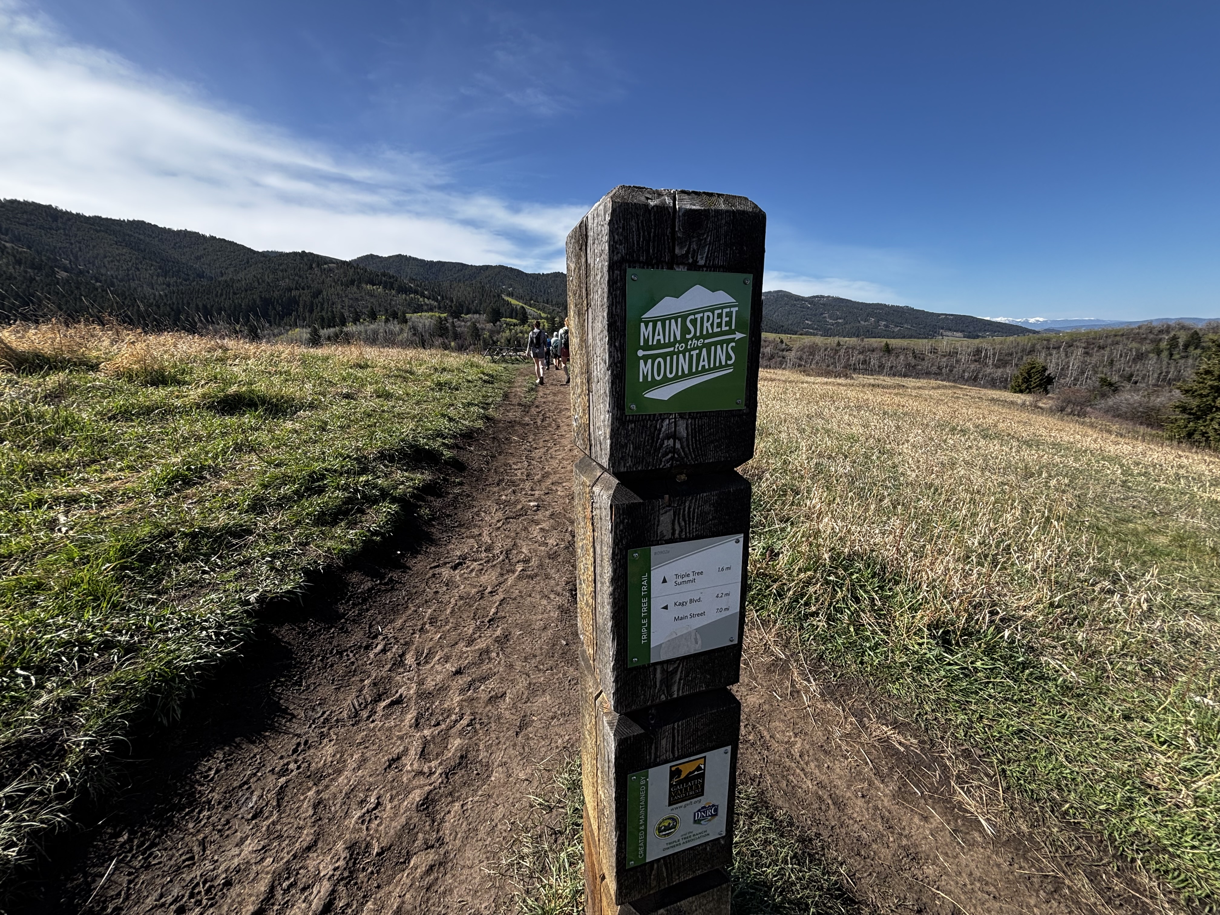 Main Street to Mountains trail marker post on the upper ridgeline with mountains and valley visible on either side
