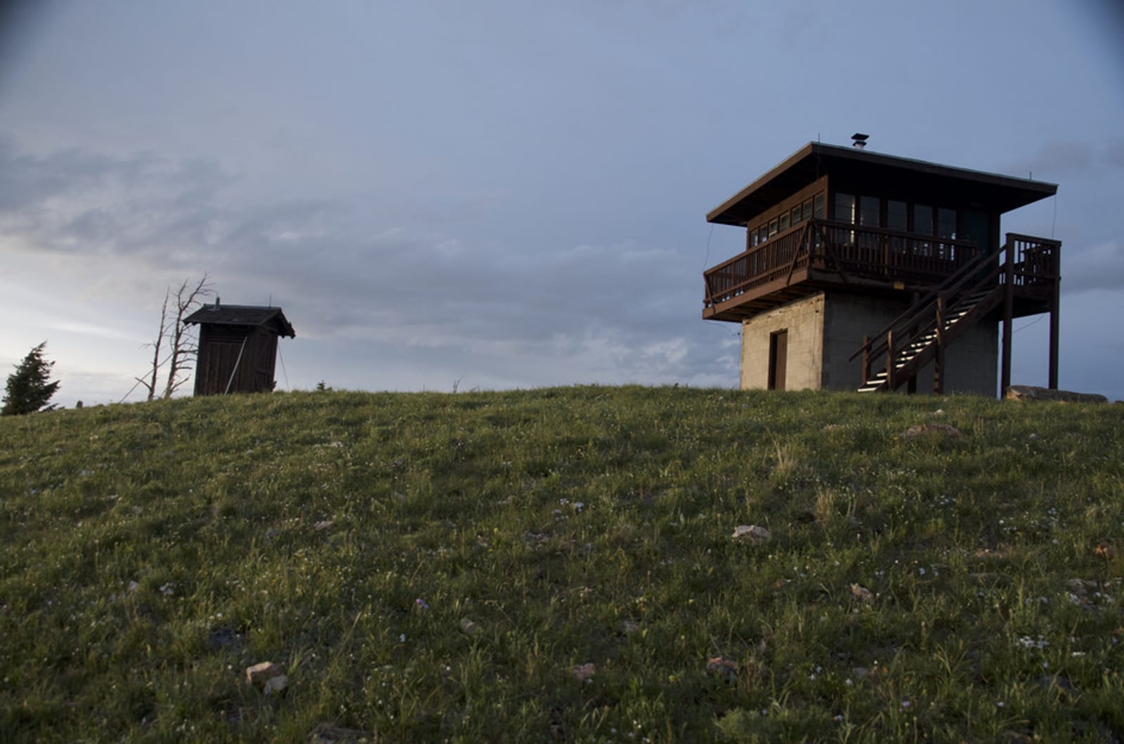 Garnet Mountain fire lookout tower with wraparound deck on grassy hilltop at dusk with outhouse in background