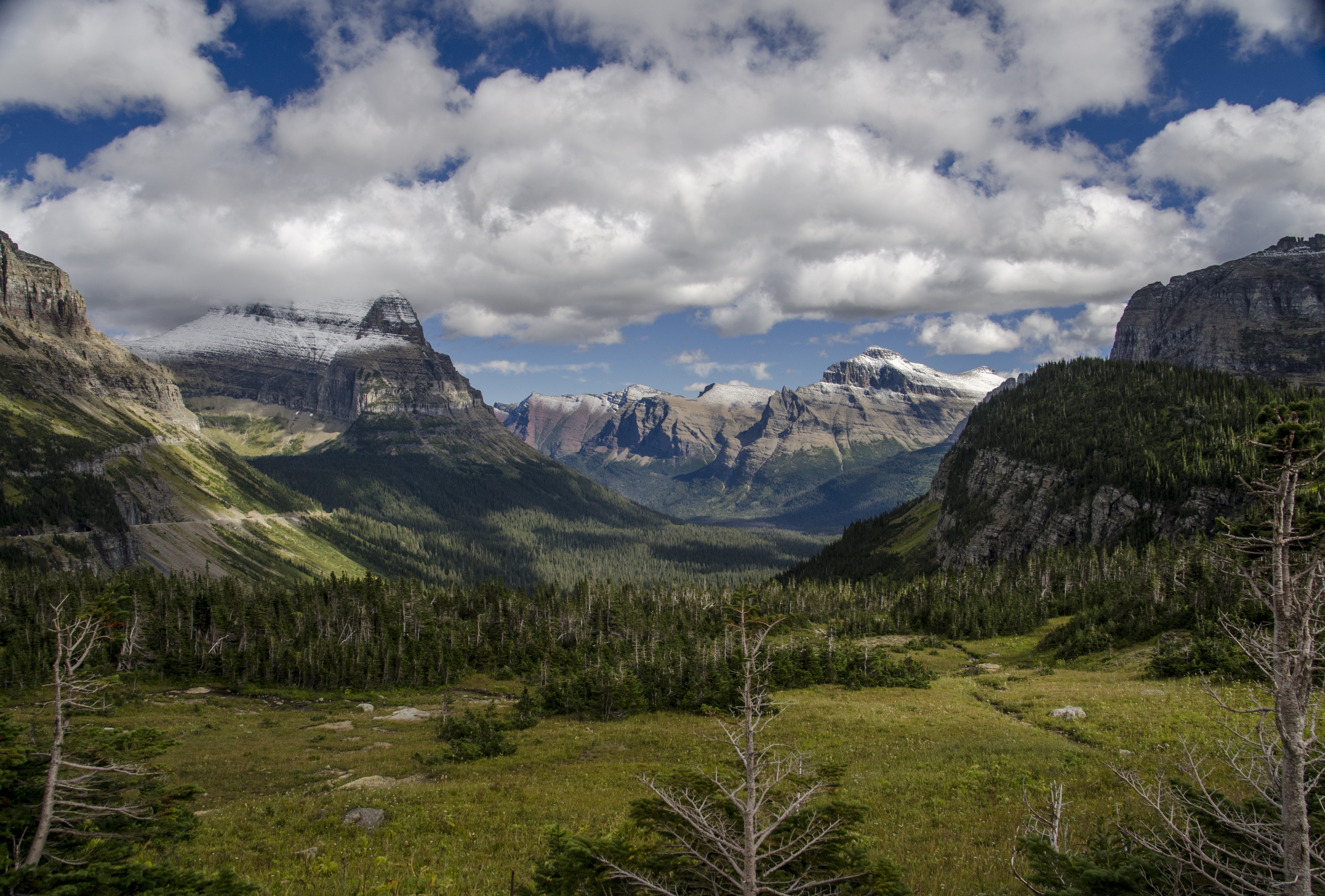 Dramatic mountain valley vista from Going-to-the-Sun Road with rugged peaks, green alpine meadows, and billowing clouds