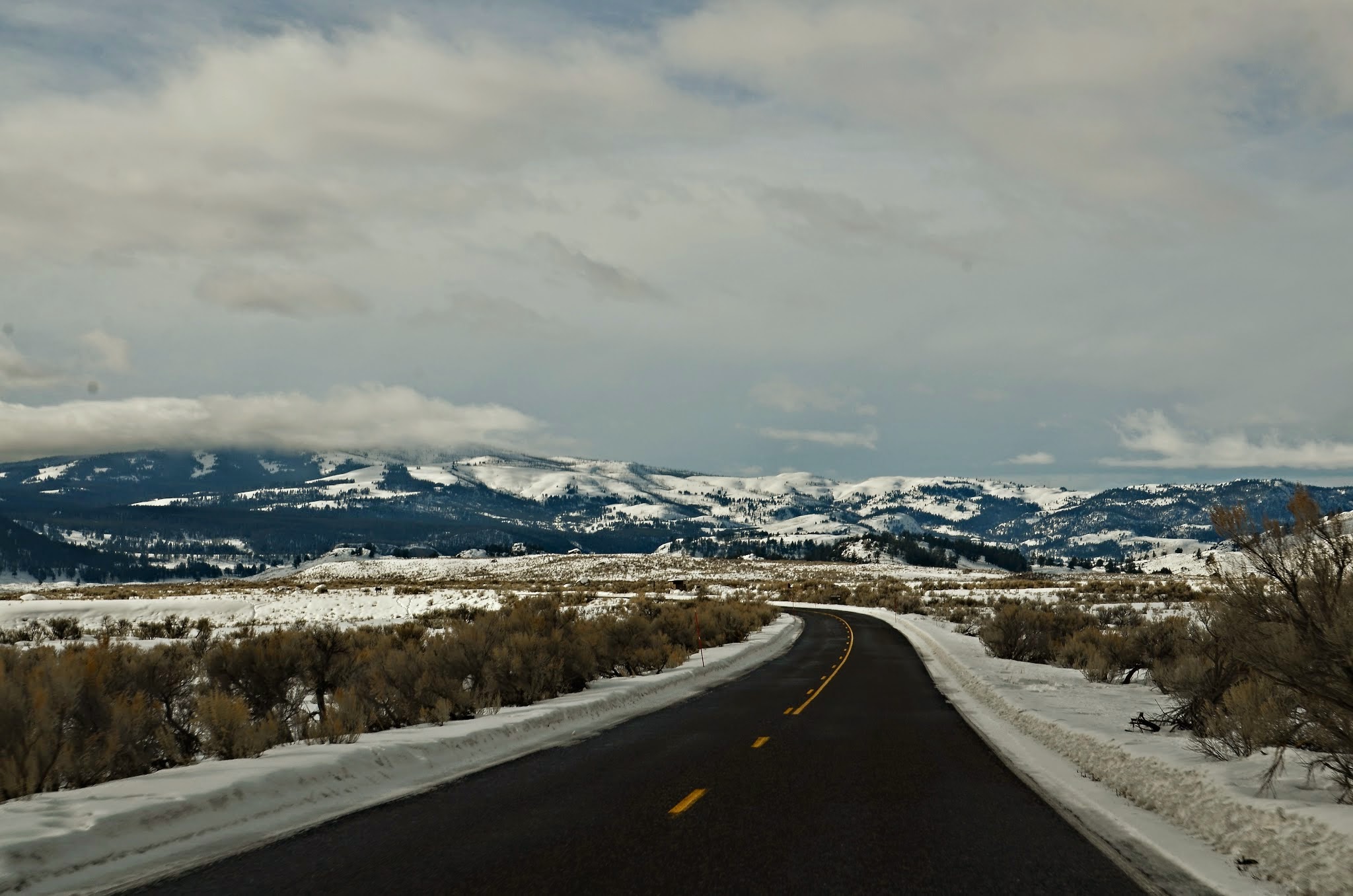 Bare winter road through Lamar Valley with sagebrush flats and snow-covered mountains ahead