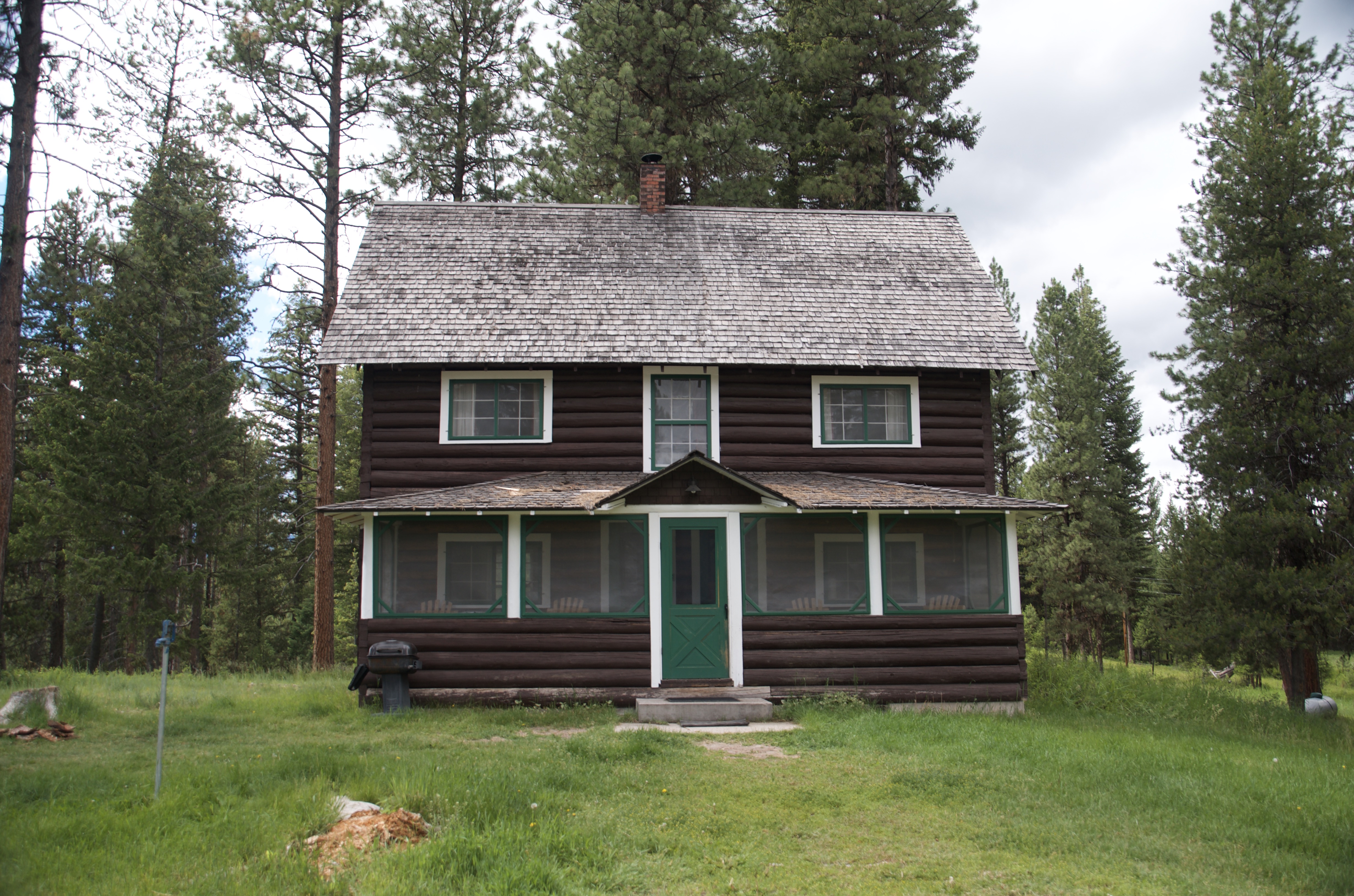 The Old Condon Ranger Station cabin, a two-story dark log cabin with green door surrounded by tall pine trees