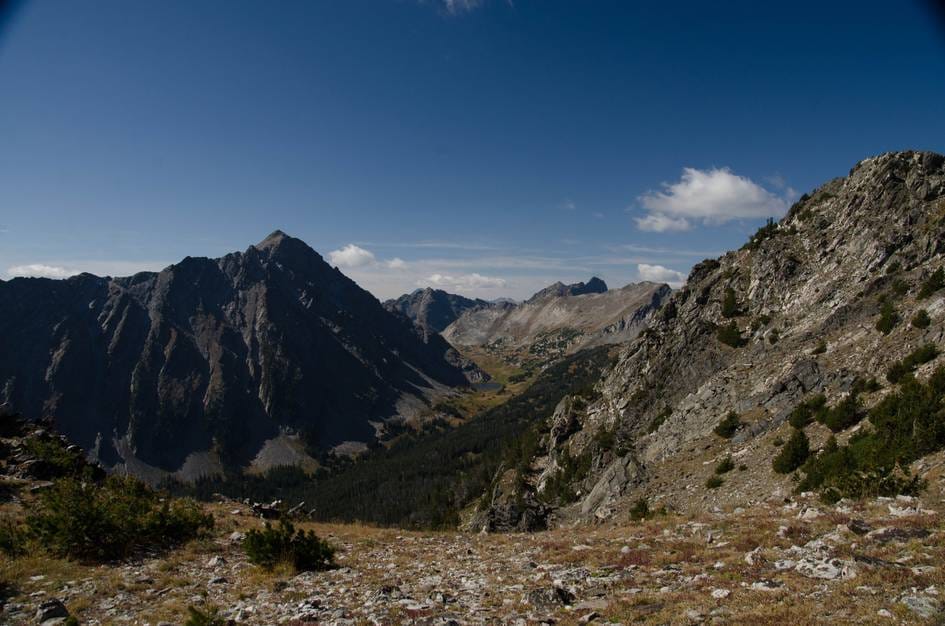 Panoramic view of Gallatin Peak and rugged Spanish Peaks mountains with Thompson Lake valley below under blue sky