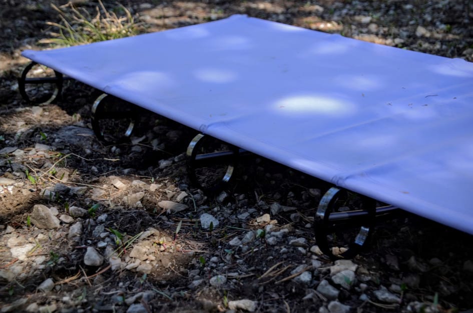 Blue ultralight backpacking cot assembled on rocky ground showing lightweight frame and fabric