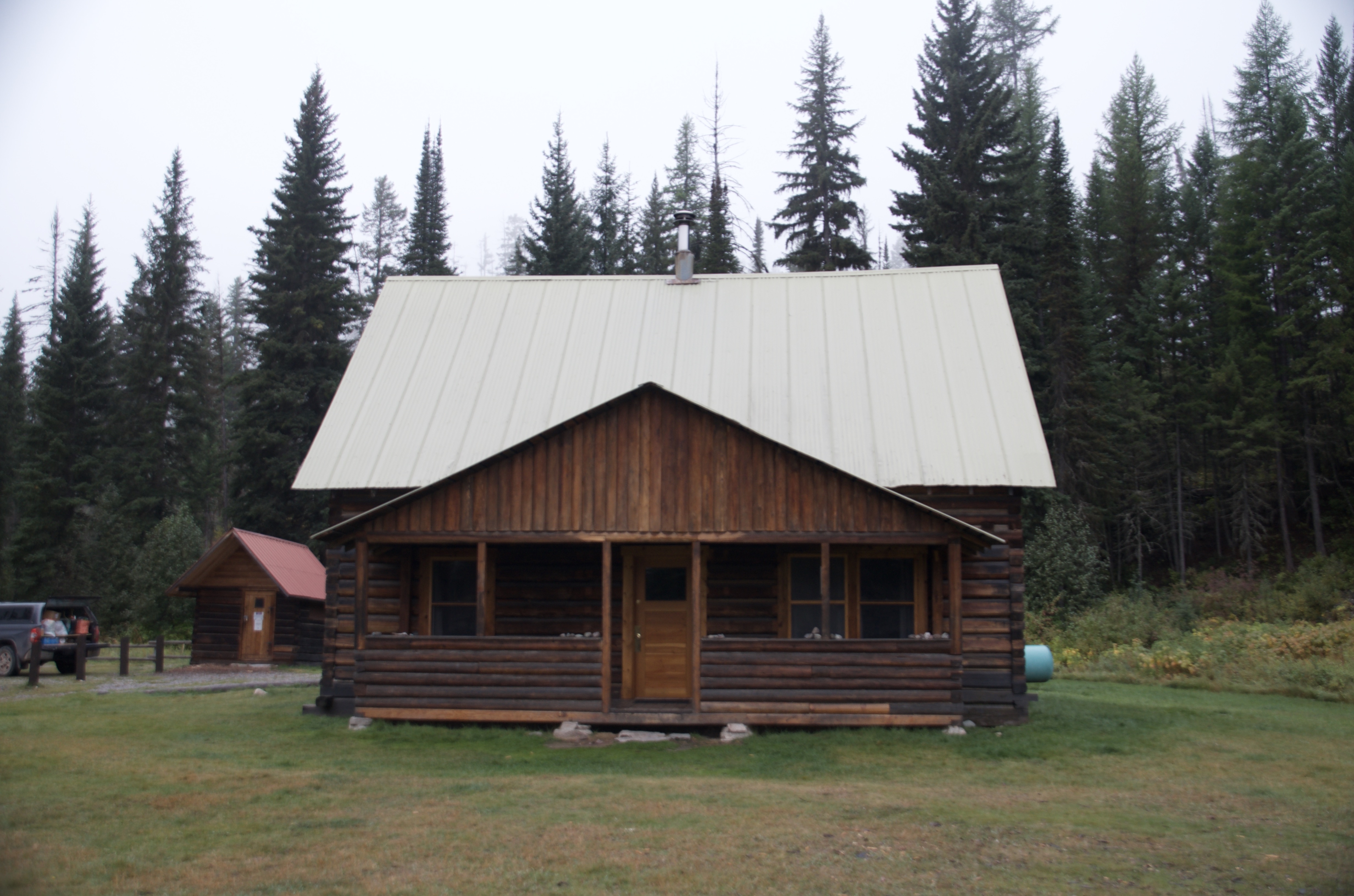 Wurtz Cabin, a two-story log cabin with covered front porch on a grassy clearing surrounded by tall pine trees